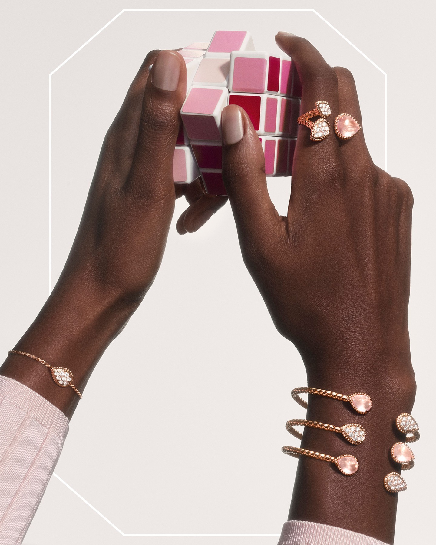 Picture of a models hands playing with a pink Rubix Cube while wearing Boucheron jewellery.